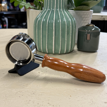 Coffee tamp with wooden handle on a light surface, with decorative vases in the background